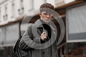 Portrait of a stylish young man with a handsome serious face with a trendy hairstyle in a checkered elegant coat with a