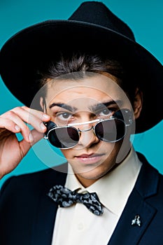 Portrait of a stylish young man in hat wearing elegant suit and sunglasses.