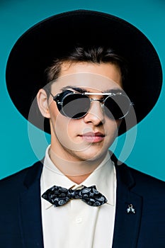 Portrait of a stylish young man in hat wearing elegant suit and sunglasses.
