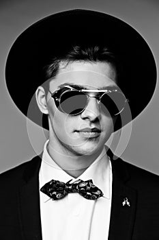 Portrait of a stylish young man in hat wearing elegant suit and sunglasses.