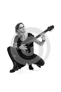 Portrait of stylish young man, rock musician, guitar player posing, playing over white background. Black and white