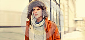Portrait of stylish young man wearing jacket with fur hood walking on the city street