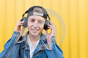 Portrait of a stylish young man who listens to music in wireless headphones on the background of a yellow wall