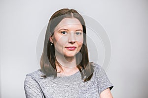 Portrait of stylish young pretty Caucasian woman smiling in grey t-shirt on white studio background, isolated, natural