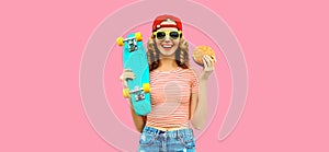 Portrait of stylish young woman with burger fast food and skateboard wearing baseball cap, sunglasses on pink background