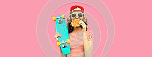 Portrait of stylish young woman with burger fast food and skateboard wearing baseball cap, sunglasses on pink background