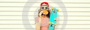 Portrait of stylish young woman with burger fast food and skateboard wearing baseball cap, sunglasses on white background