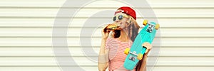 Portrait of stylish young woman with burger fast food and skateboard wearing baseball cap, sunglasses on white background