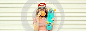 Portrait of stylish young woman with burger fast food and skateboard wearing baseball cap, sunglasses on white background