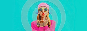 Portrait of stylish young woman in headphones listening to music blowing her lips sends sweet air kiss wearing colorful pink