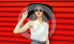 Portrait stylish young woman model posing wearing black summer straw round hat on red background