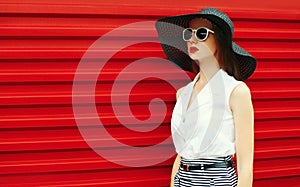 Portrait stylish young woman model posing wearing black summer straw round hat on red background