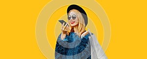 Portrait of stylish young woman with shopping bags and smartphone using voice command recorder, assistant or takes calling in city