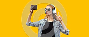 Portrait of stylish young woman taking selfie with smartphone in wireless headphones listening to music and blowing her lips sends