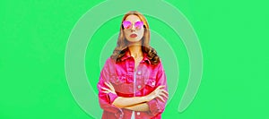 Portrait of stylish young woman wearing pink jacket, sunglasses on green background