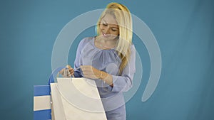 Portrait of stylish young women looking into paperbag with new clothes at isolated blue background. Shopoholic shopping