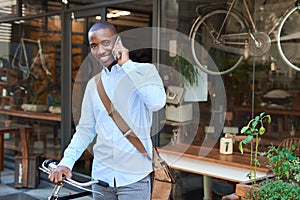 Smiling man standing with a bike talking on a cellphone