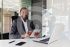 Portrait of successful African American businessman inside office, boss with tablet computer smiling and looking at