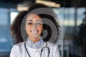 Portrait of successful African American female doctor, with stethoscope around neck, standing in modern clinic, smiling