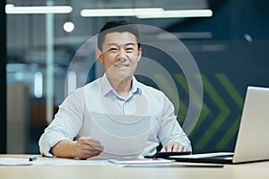 Portrait of successful asian boss, man with document in modern office