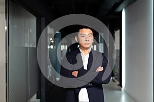 Portrait of a successful Asian manager boss, with crossed arms in a business suit looking pensively at the camera, serious man in