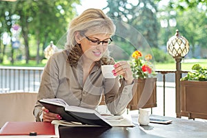 Portrait of successful beautiful middle-aged blonde woman in summer outdoor restaurant