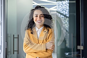 Portrait of successful business woman inside office, latin american boss in yellow suit smiling and looking at camera