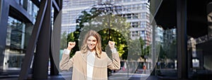 Portrait of successful business woman, young corporate woman celebrating victory, achievement, triumphing on street