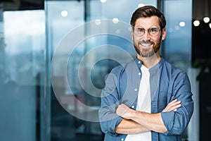 Portrait of successful businessman inside modern office, mature man with beard and glasses smiling and looking at camera