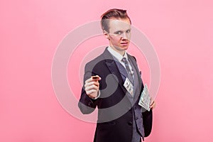 Portrait of successful conceited rich businessman offering money at camera. studio shot isolated, pink background photo