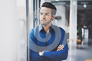 Portrait of successful confident hispanic businessman standing close from the window in modern office.Horizontal,blurred