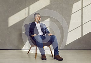 Portrait of successful confident mature businessman sitting on chair by grey office wall