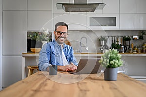 Portrait of successful entrepreneur with laptop on desk sitting at home office, smiling at camera