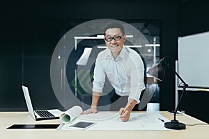 Portrait of successful and experienced Asian architect, man standing over table with plan
