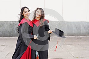 Portrait of successful graduate female students wearing cap outdoors near university