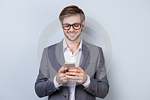 Portrait of successful handsome young man in formal wear with beaming smile, bristle and glasses holding smartphone and