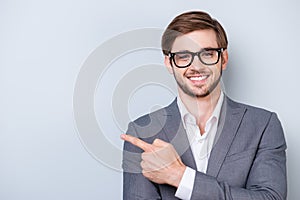 Portrait of successful handsome young man in formal wear with beaming smile, bristle and glasses pointing to the side