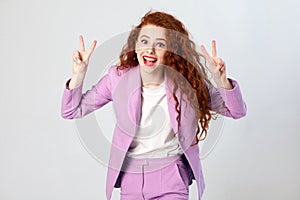 Portrait of successful happy beautiful business woman with red - brown hair and makeup in pink suit showing v sign or peace.