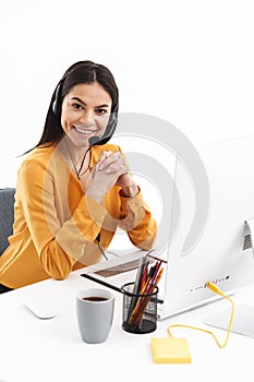 Portrait of successful hotline assistant woman wearing microphone headset speaking with customer by phone in office