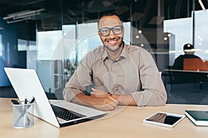 Portrait of successful investor, african american man smiling and looking at camera, man working inside office using