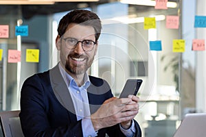 Portrait of successful man in business suit in office interior, mature businessman smiling and looking at camera