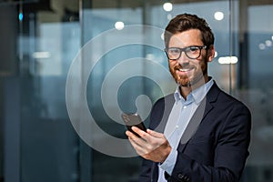 Portrait of successful mature businessman investor, man in glasses and beard smiling and looking at camera, boss in suit