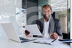 Portrait of successful mature experienced financier, business man behind paper work smiling and looking at camera