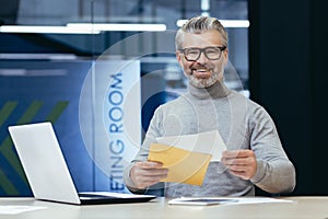 Portrait of successful mature financier, senior gray haired businessman smiling and looking at camera at workplace, boss