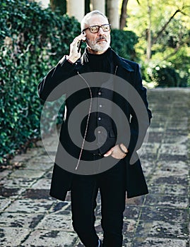Portrait of successful middle age businessman talking on his smartphone while walking in city park.Vertical,blurred