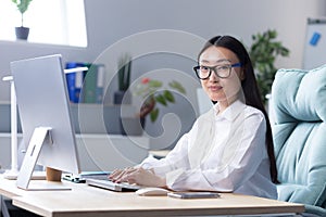 Portrait of successful office worker Asian woman, looking at camera smiling, business woman in glasses working and