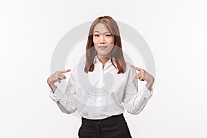 Portrait of successful professional and confident asian woman in white shirt, pointing herself and smiling pleased