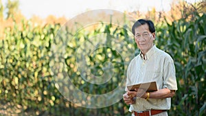 Portrait of successful senior male farmer standing in corn field. Agribusiness concept