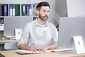 Portrait of a successful and serious businessman, pensive man looking at the camera working in the office at the computer