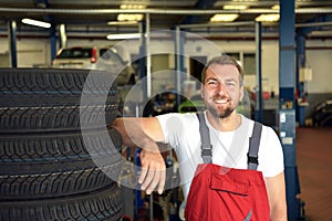 Portrait of successful smiling car mechanic in a workshop on a stack of tires at his workplace